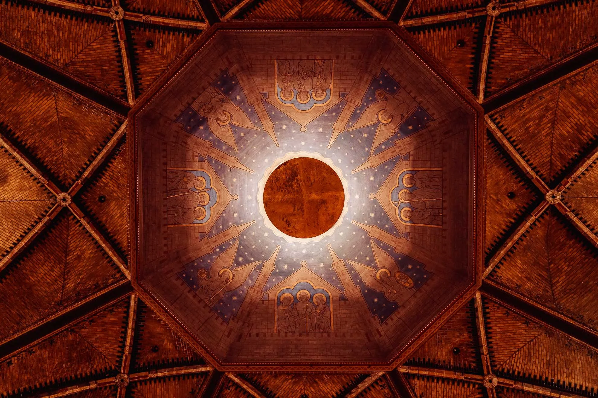 Interior view of a vaulted wooden ceiling with artwork and intricate designs, featuring a central circular element and decorative patterns.