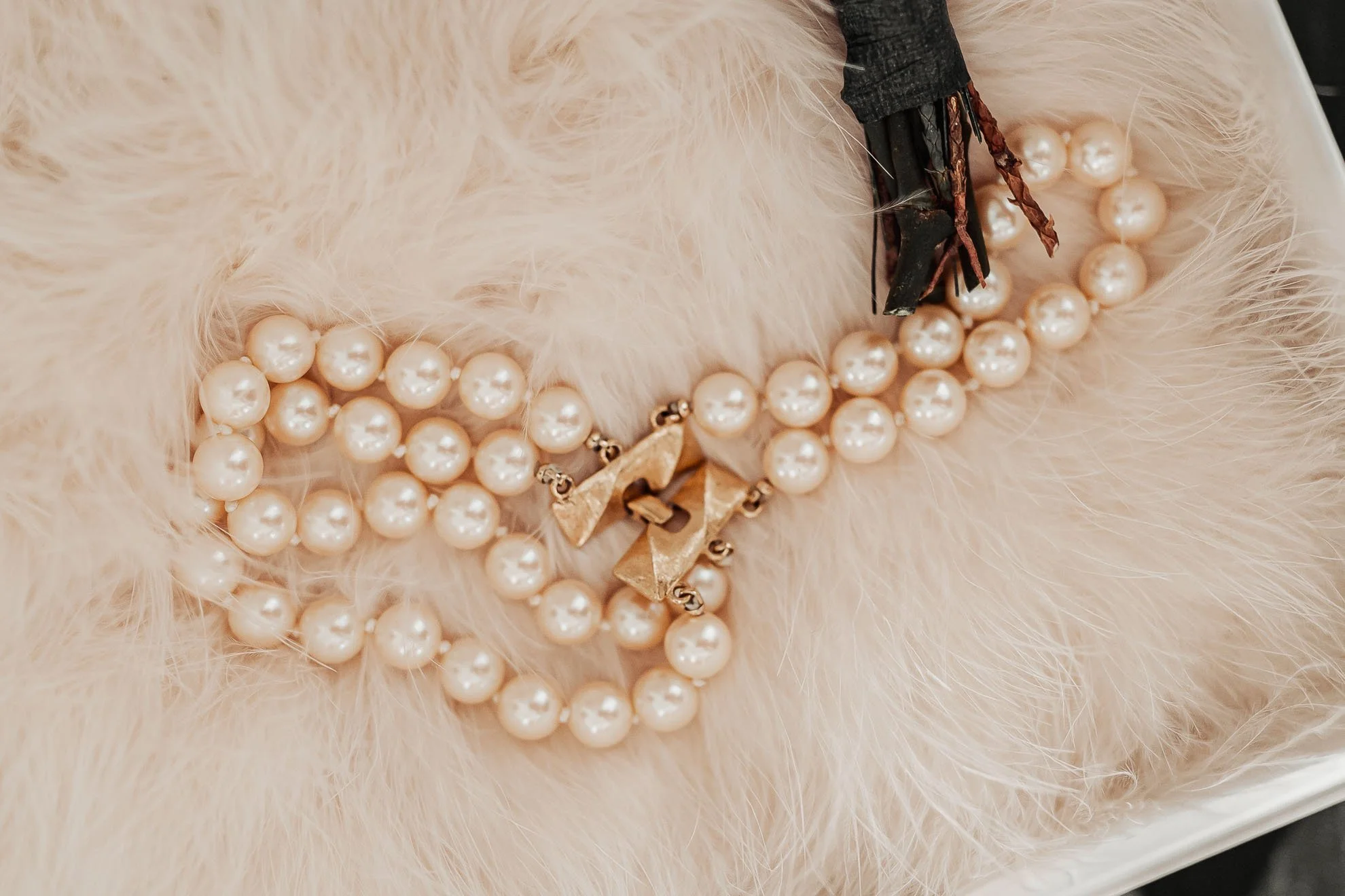 Close-up photo of a string of pearl necklaces with a black decorative bow, placed on soft, white, fluffy furry fabric.
