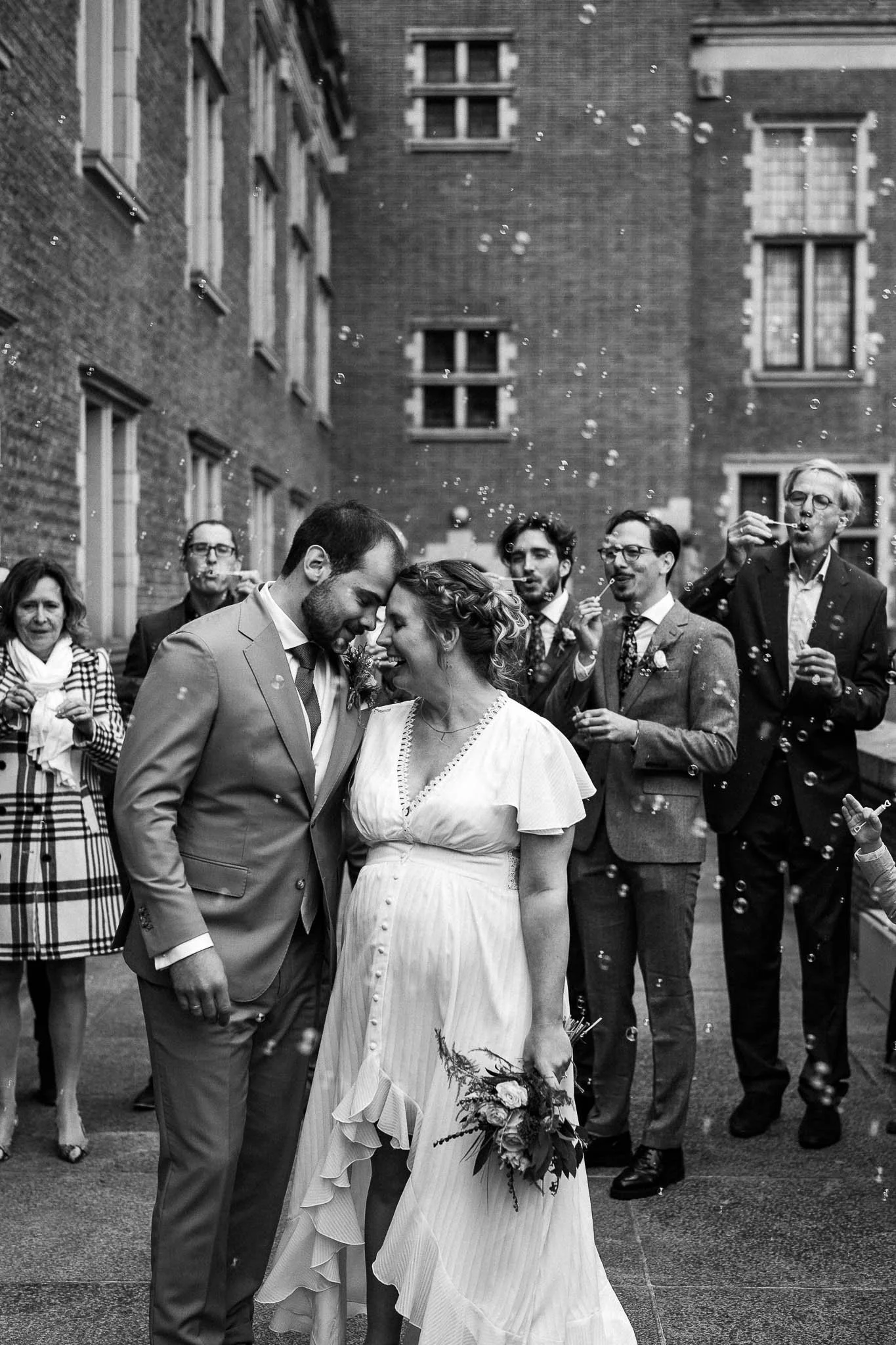 Een zwart-witfoto van een bruiloft met een bruid en bruidegom die dicht tegen elkaar staan, omringd door familie en vrienden die belletjes blazen.
