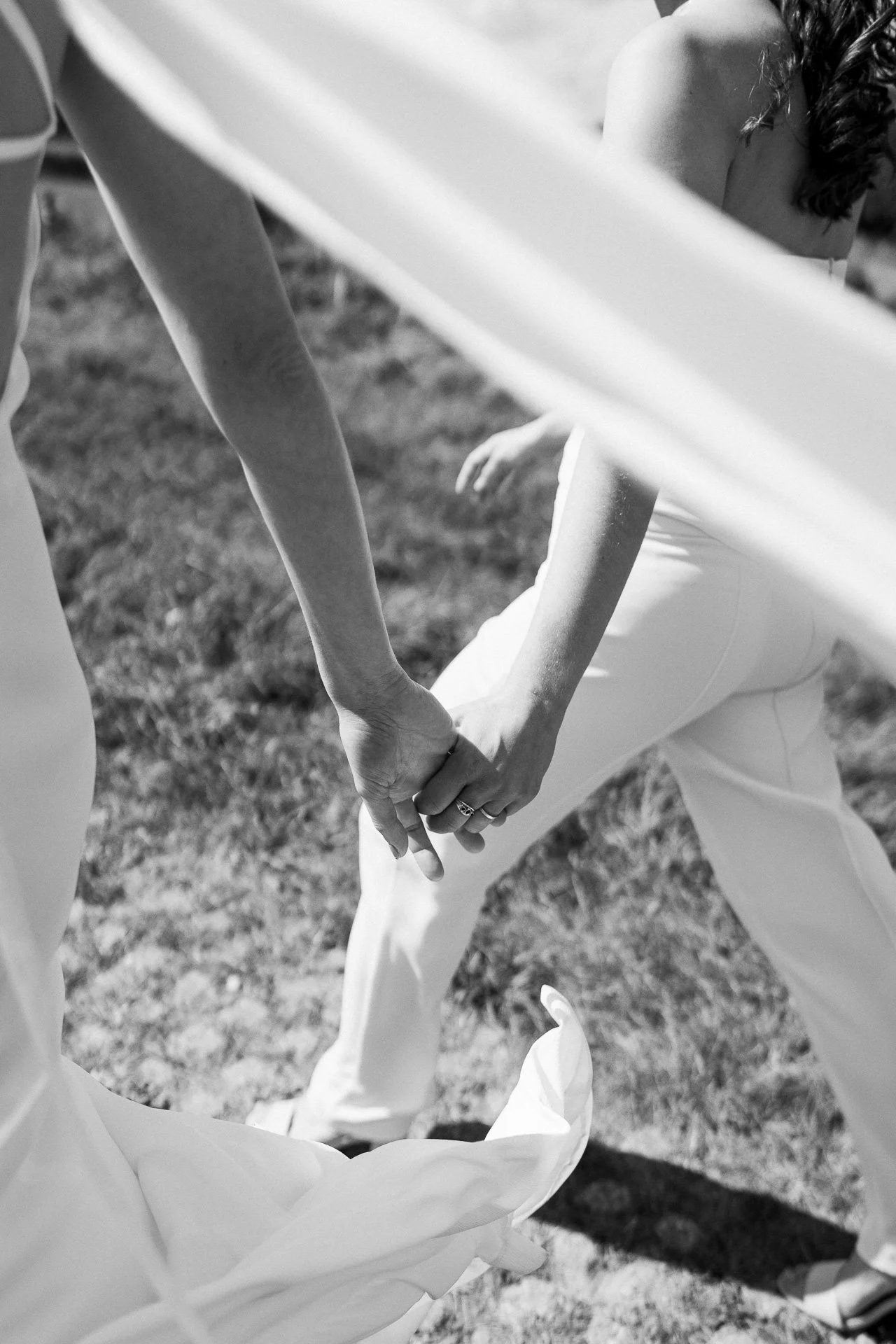 Twee mensen die hand in hand vasthouden, zittend op gras, zwart-wit foto.