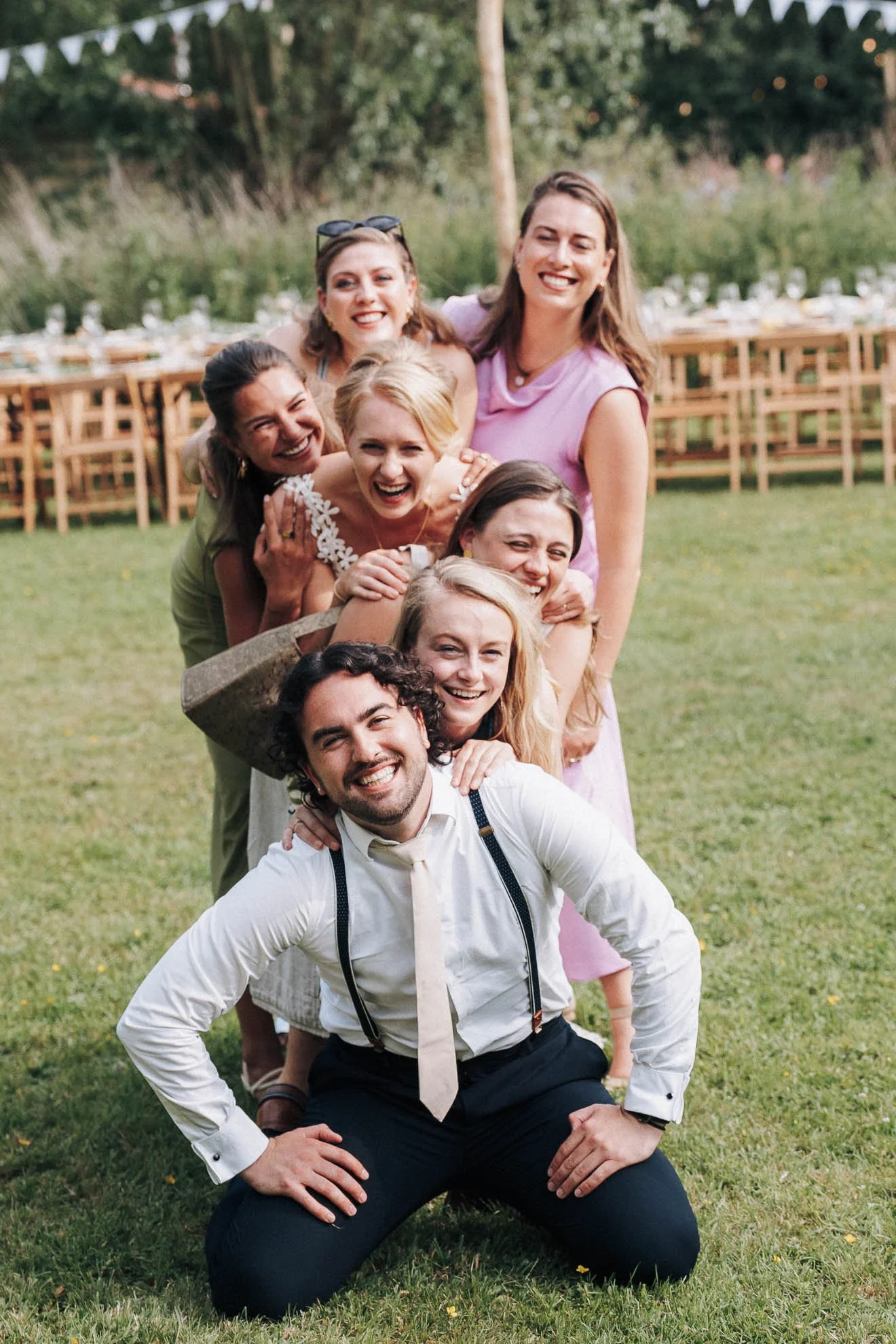 Group of friends forming a human pyramid outdoors on a grassy field during daylight, smiling and having fun.
