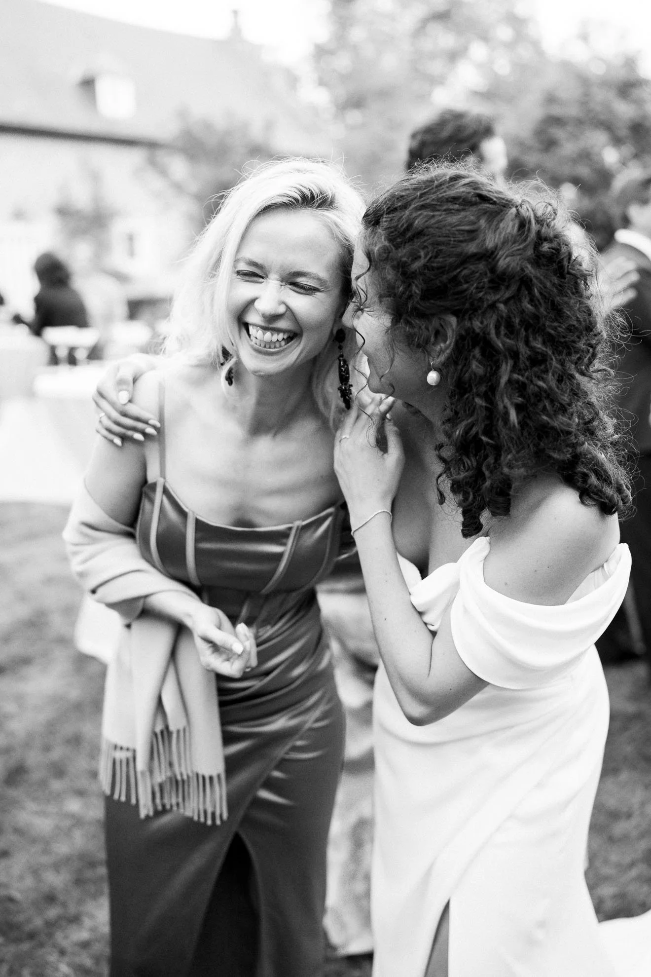 Two women sharing a joyful moment, smiling and leaning into each other at an outdoor event, black and white photograph.