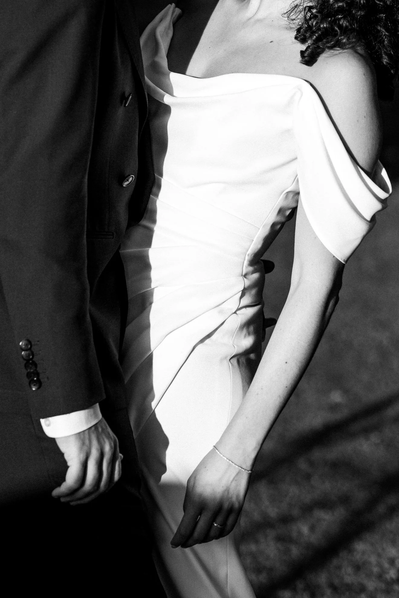 A close-up black and white photo of a man in a suit and a woman in a dress, sitting together with their hands touching.