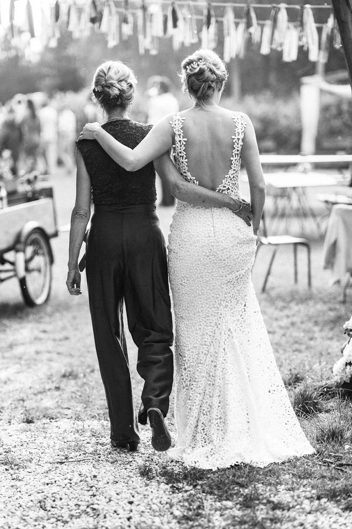 Twee vrouwen lopen hand in hand, een lijkt de bruidsjurk te dragen, tijdens een bruiloft buiten.