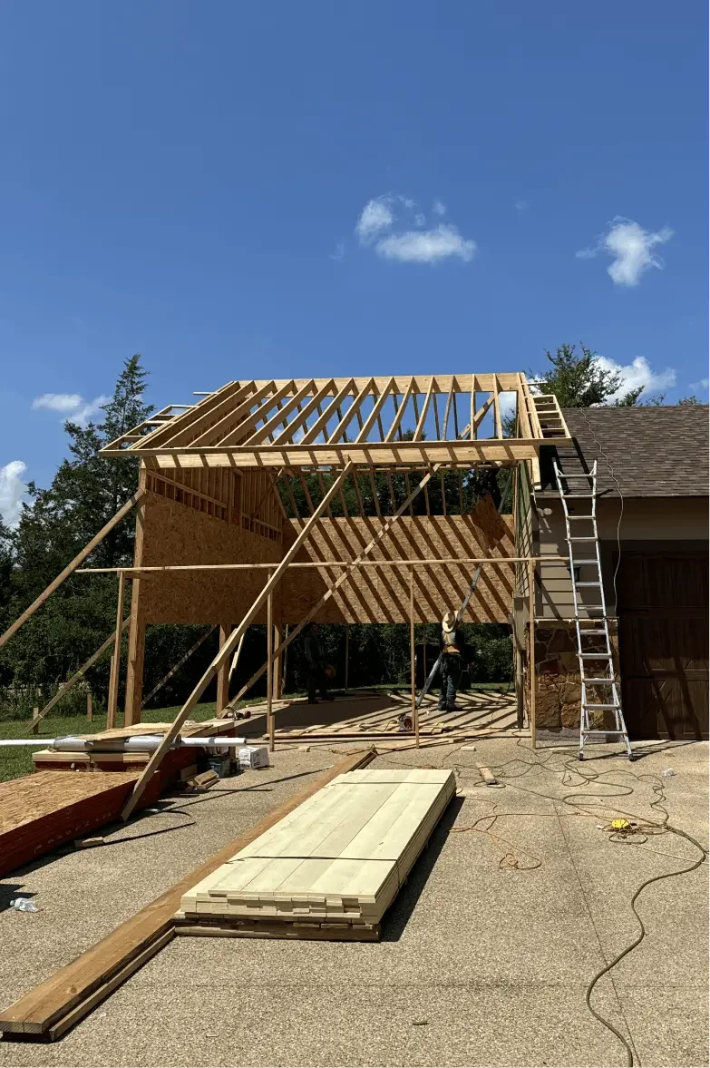 Construction of a new wooden structure attached to a garage on a clear, sunny day.