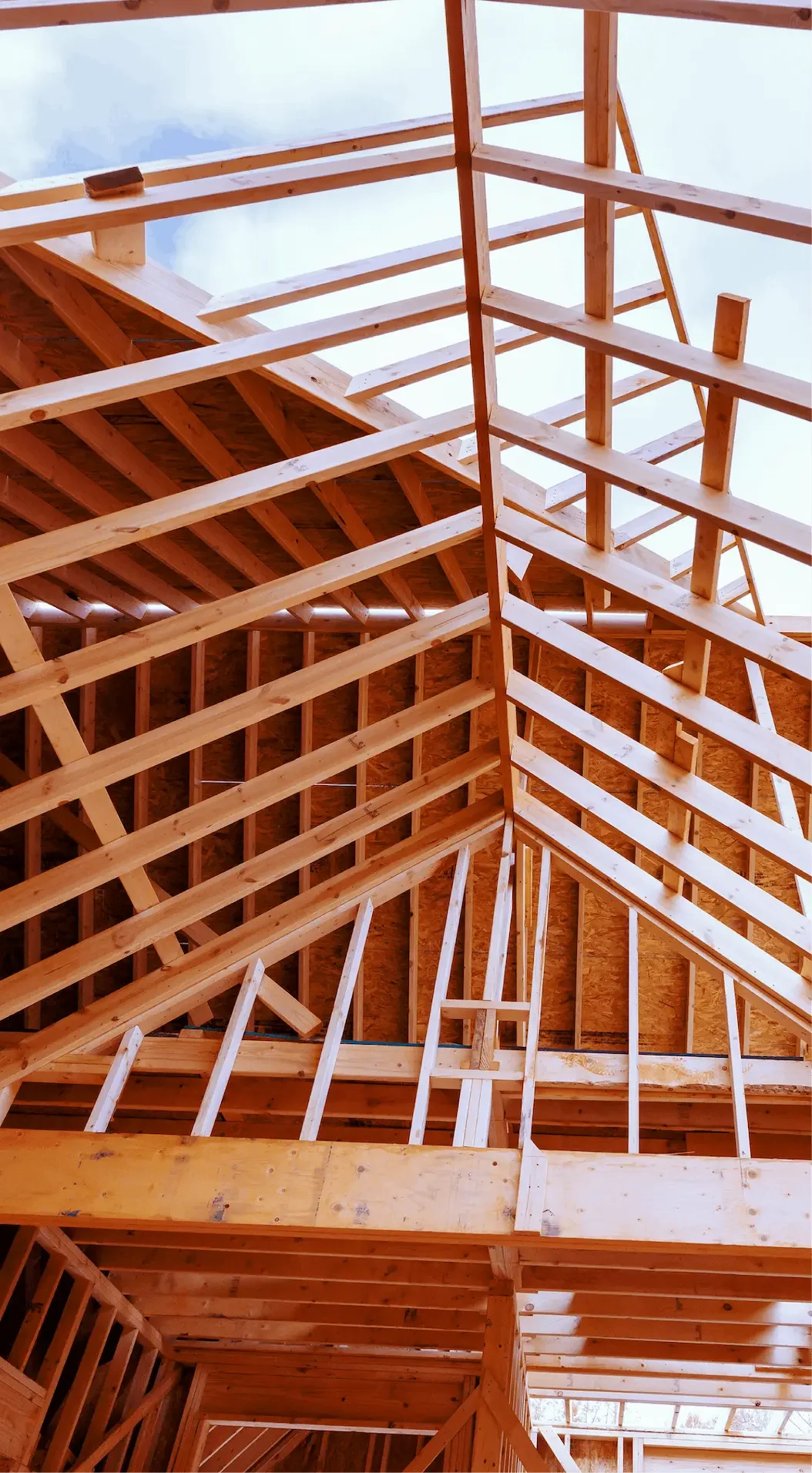 The image shows the wooden framework of a building under construction, including roof and wall support beams, with the sky visible through the unfinished roof.
