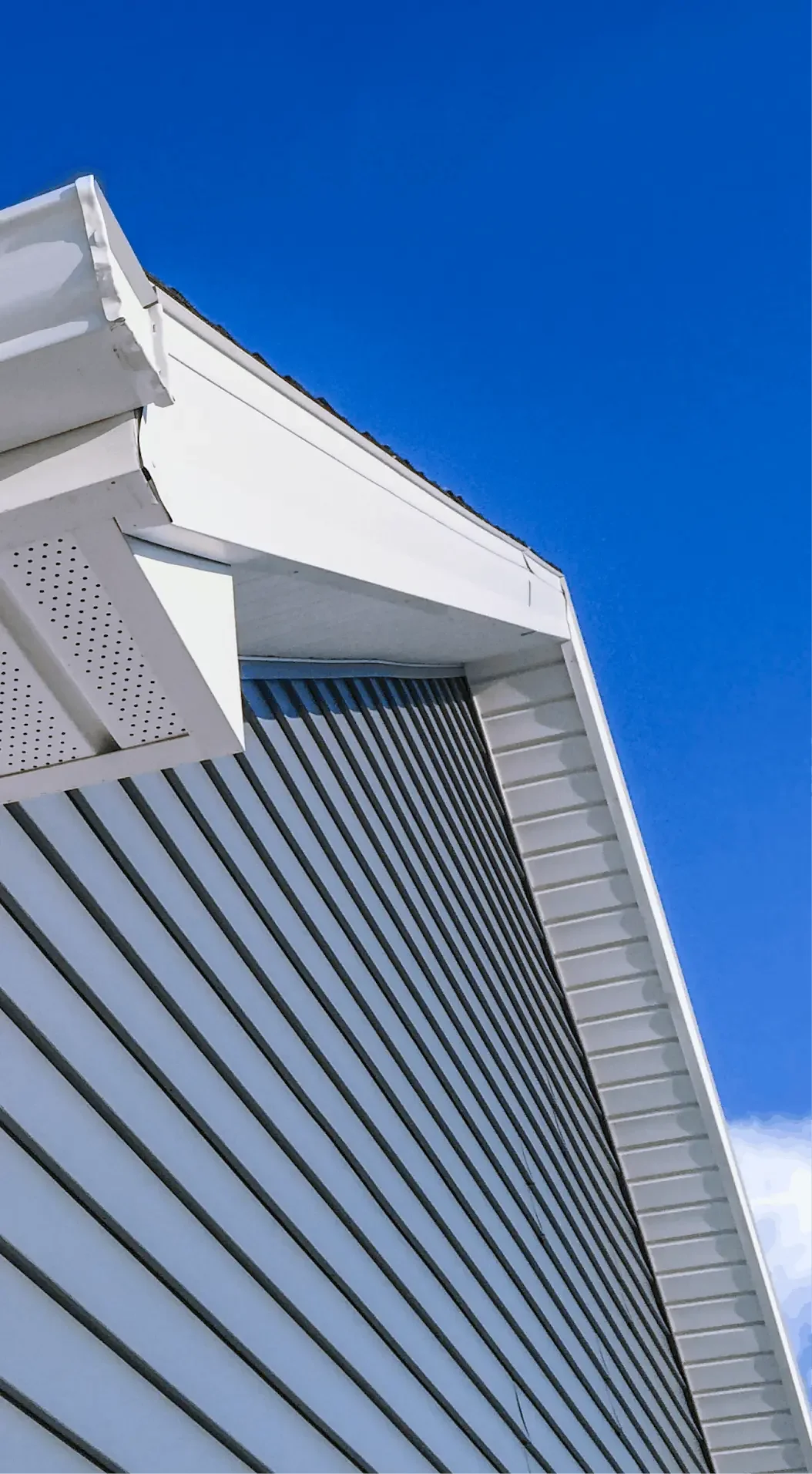 Close-up of the side of a modern building with horizontal metal louvers and white trim, against a clear blue sky.