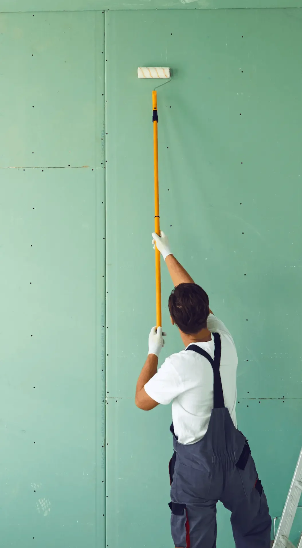 Person using a paint roller to paint a green wall.