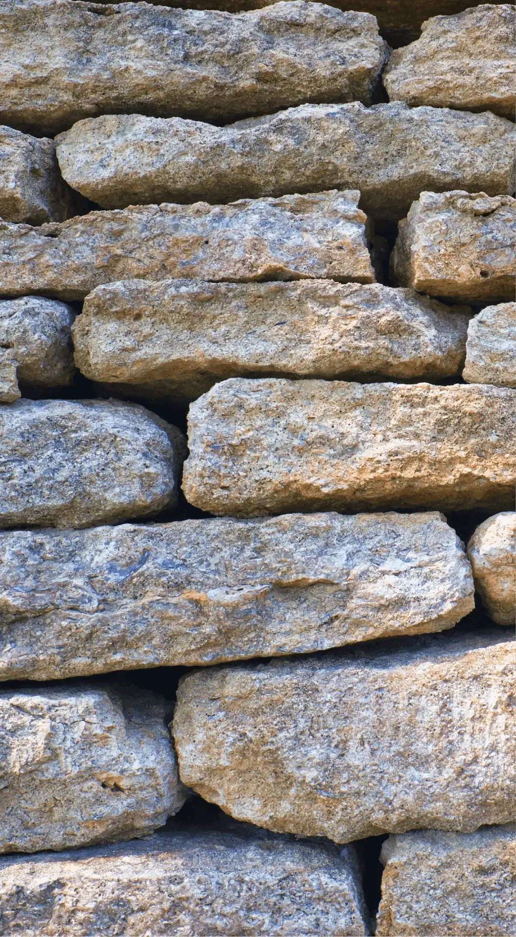 Close-up of a stacked stone wall made of rough, beige and gray stones.