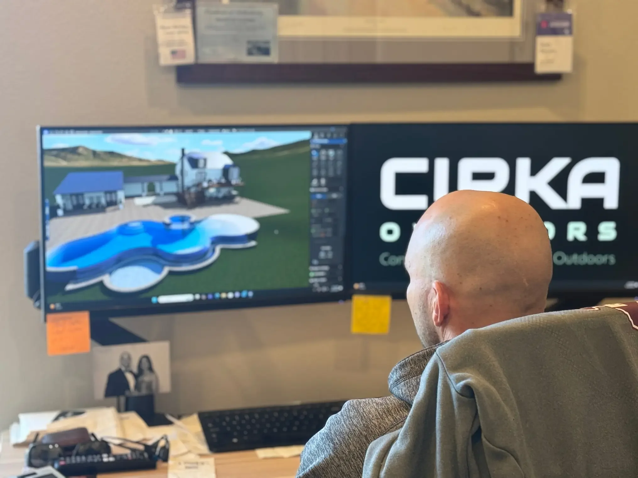 Person working on computer with landscape design on screen, in an office setting.