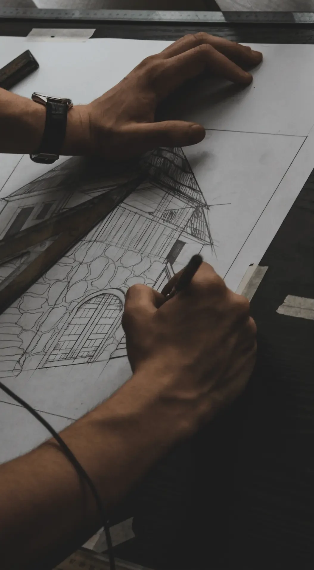 Hands sketching a detailed architectural drawing of a house with a gabled roof, on a white sheet of paper.