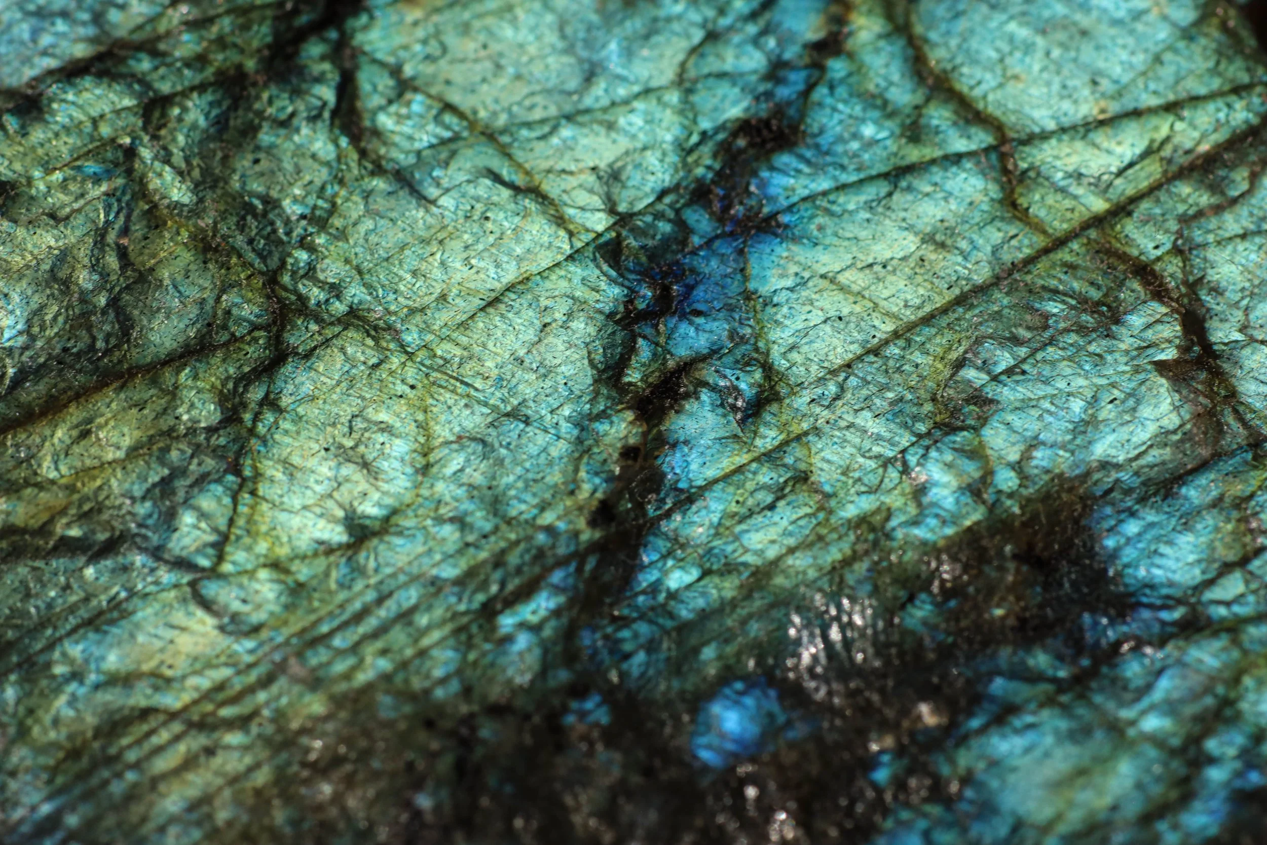 Close-up of labradorite: a greenish-blue textured surface with black lines and iridescent highlights.