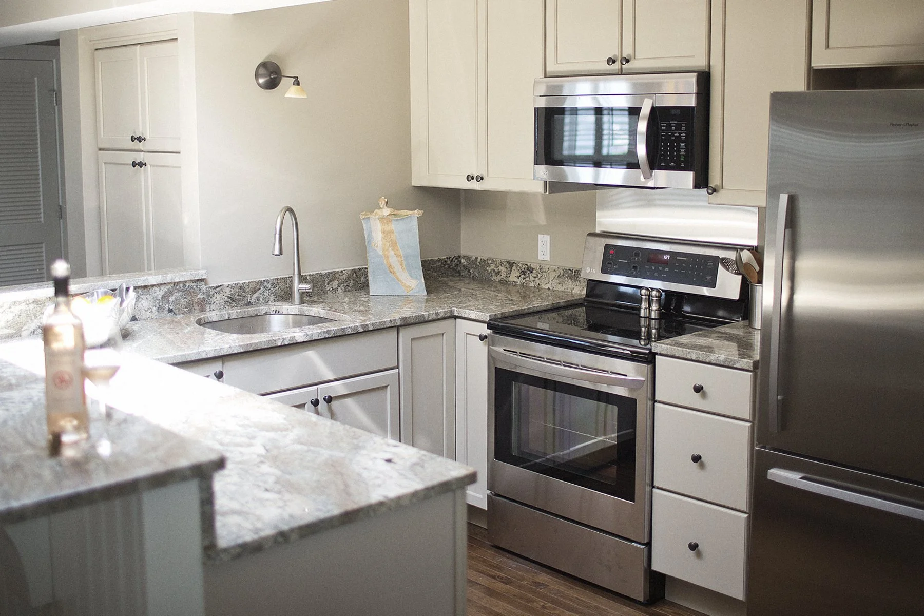Kitchen with cream-colored cabinets, granite countertops, stainless steel appliances including a stove, microwave, and refrigerator, and a single-basin sink with a faucet.