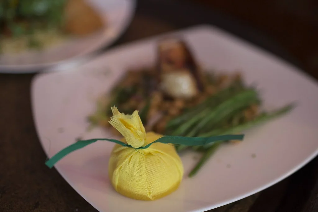 Small yellow fabric pouch tied with a green ribbon in front of a plate of food.