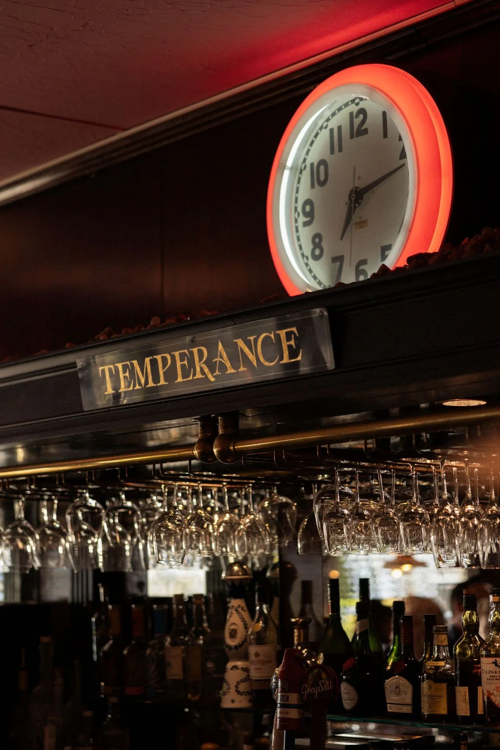 A clock showing 2:10 hangs above a bar with hanging wine glasses and bottles, with a sign reading 'TEMPERANCE' below it.