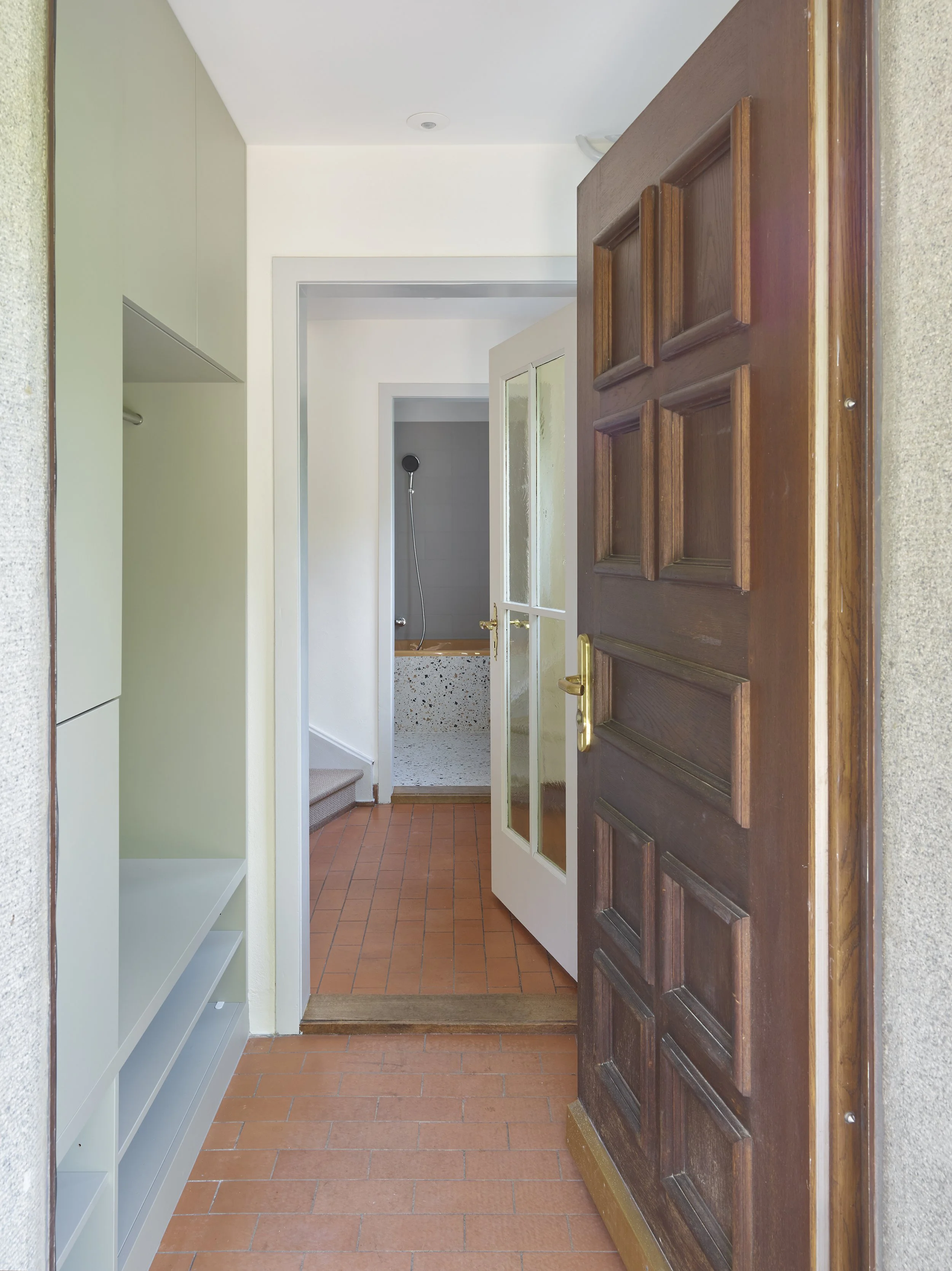 Offene Haustür führt in eine kleine Diele mit Flur, Toilette und Dusche, die Terrasse und Garten sind sichtbar.