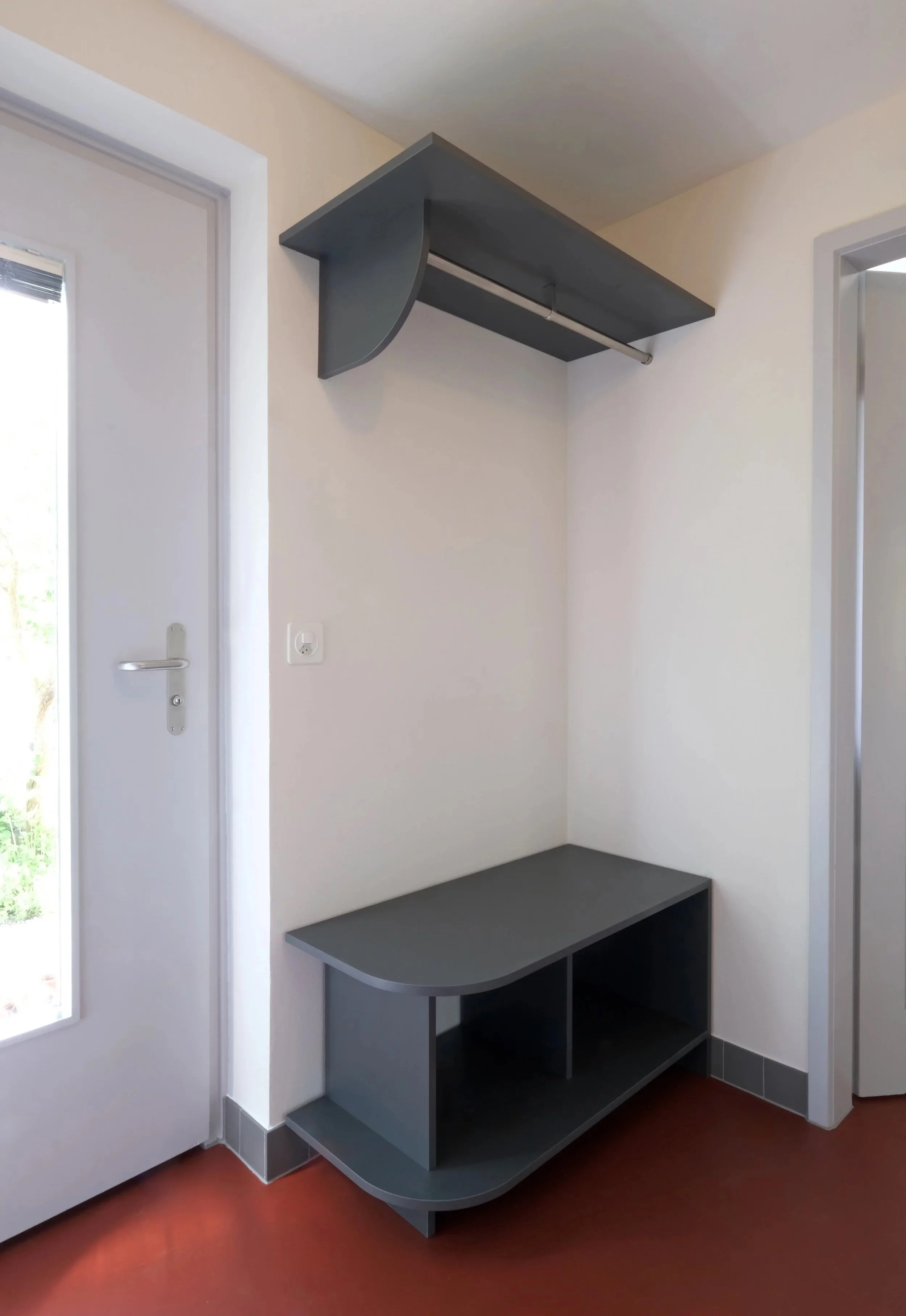 Ein Flur mit weißer Wand, einer dunklen Ablage mit Stauraum und einer schwarzen Wandlampe, daneben eine Tür mit Fenster