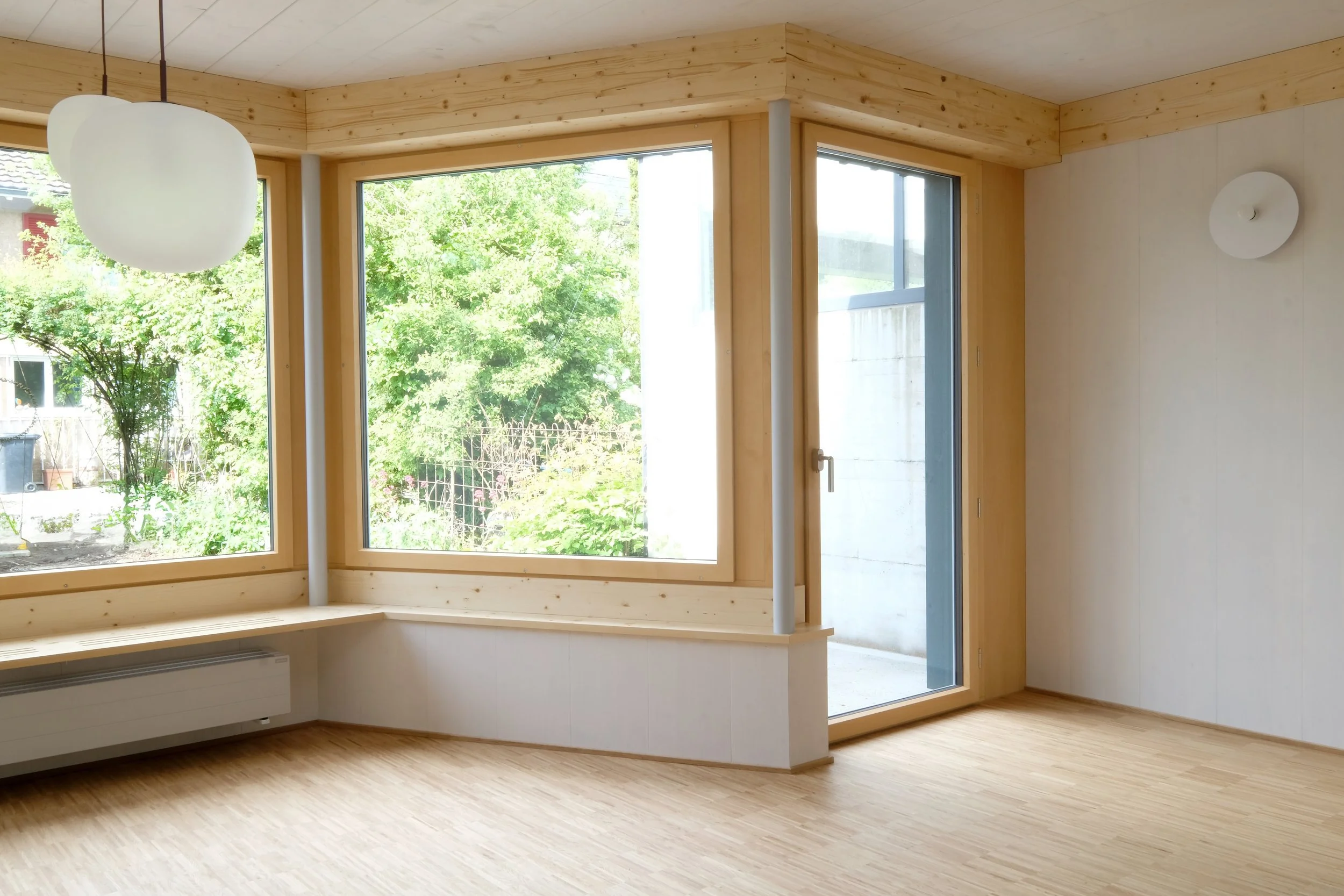 Innenraum eines modernen Zimmers mit großen Fenstern, Holzbalken, Holzfußboden und leisem Tageslicht.