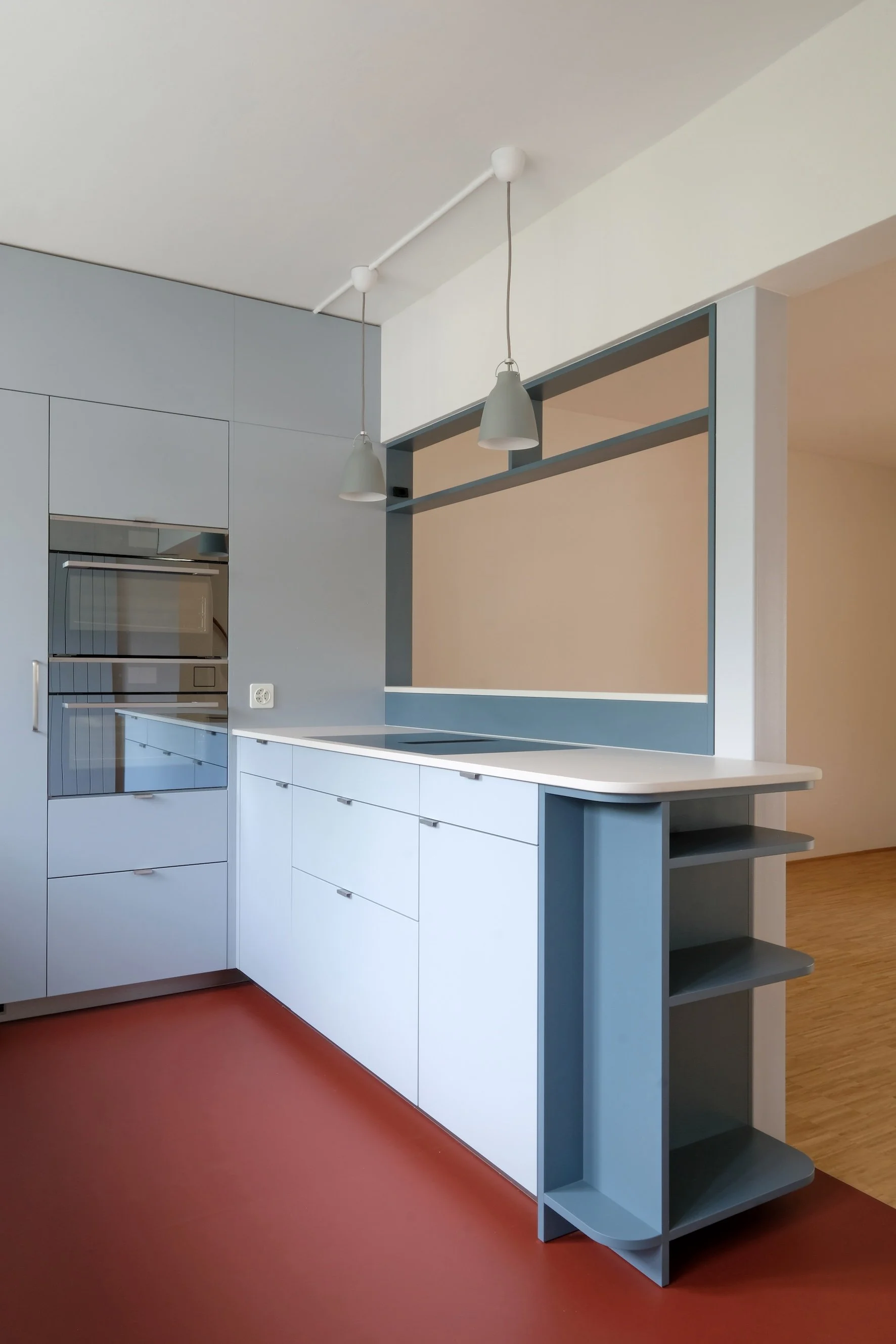Moderne Küche mit weißen Schränken, blauen offenen Regalen, grauen Pendelleuchten und einer roten Bodenfläche.