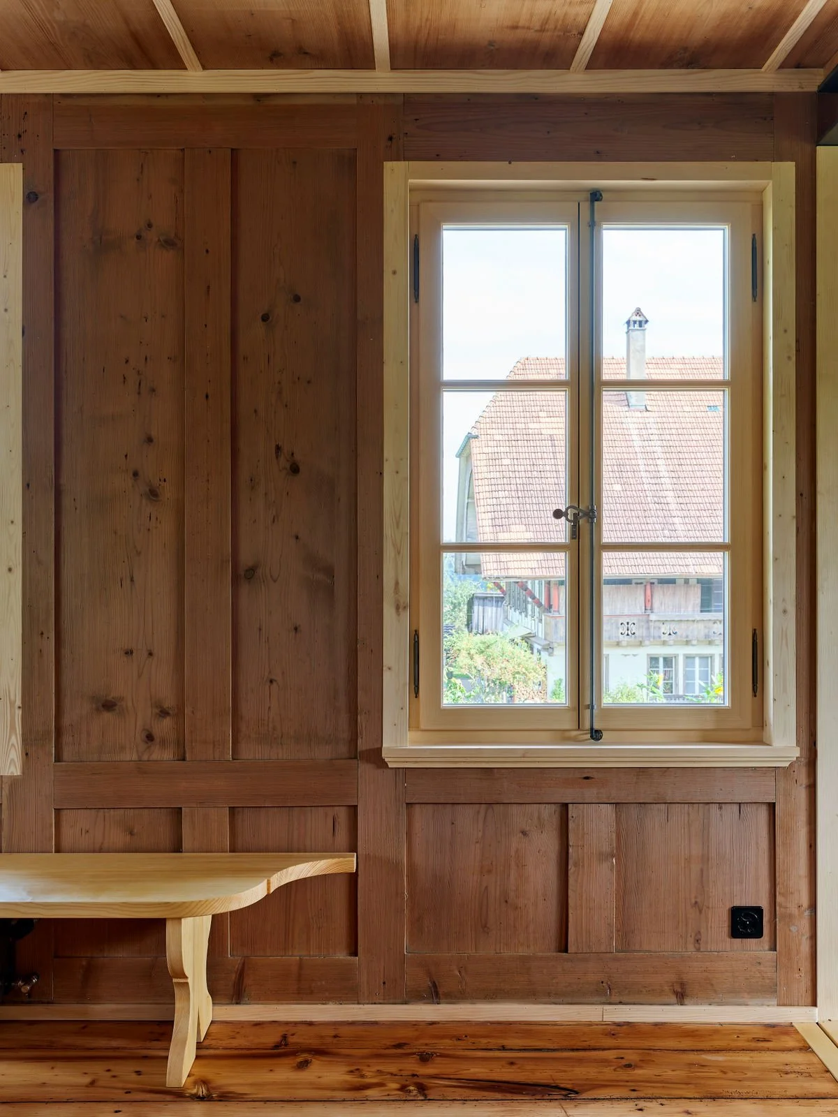 Fenster in einem Holzraum mit sichtbarer Holzvertäfelung und einem kleinen Holztisch im Vordergrund.