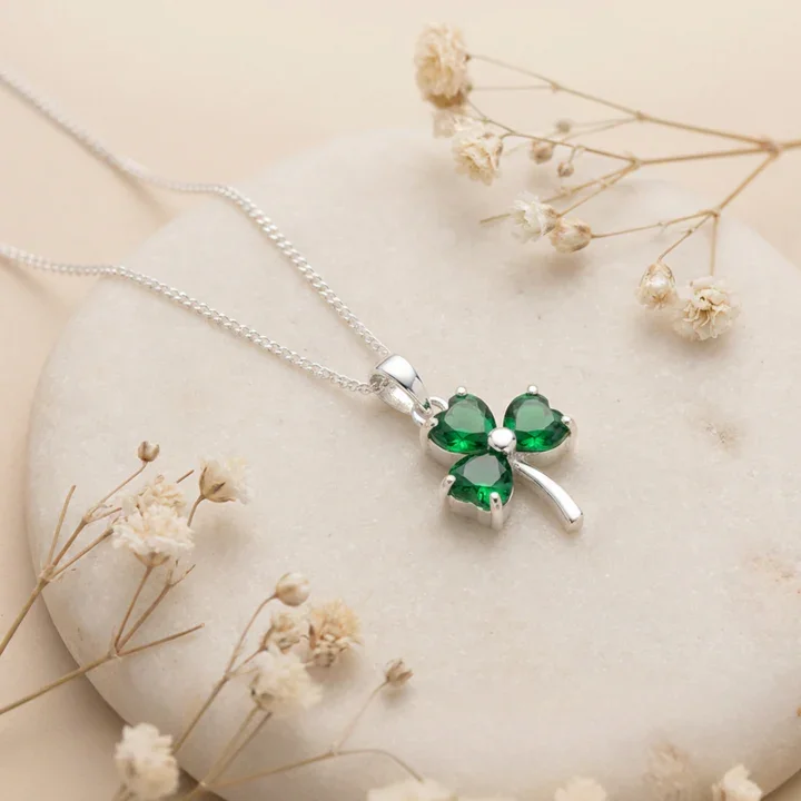 Sterling Silver Irish Shamrock Pendant, green CZ heart-shaped stones, claw set, shown on sea stone with dried botanicals