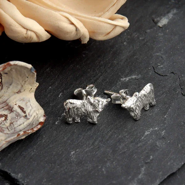 Sterling Silver Scottish Highland Cow Stud Earrings, sculpted form, engraved coat detail, 12mm x 7mm, push back fitting, shown on Scottish slate with sea stones and dried botanicals