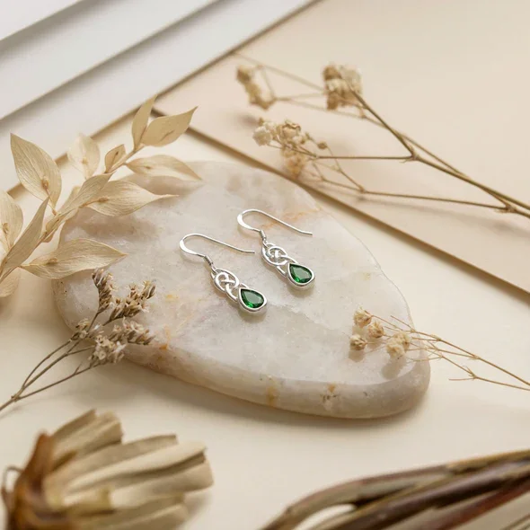 Sterling Silver Celtic Knotwork Drop Earrings, pear-cut green stone bezel set, fish hook fitting, shown on sea stone with dried botanicals