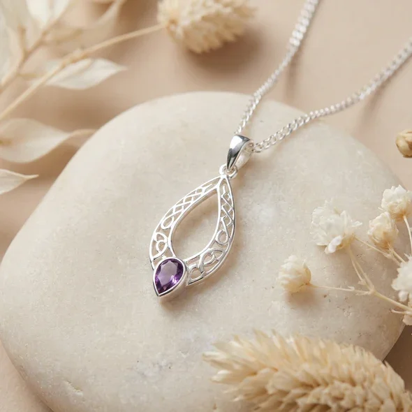 Sterling Silver Celtic Knotwork Navette Pendant, pear-cut amethyst claw set, shown on sea stone with dried botanicals