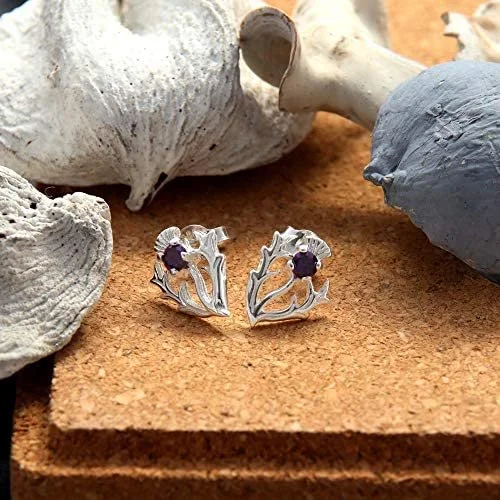 Sterling Silver Scottish Thistle Stud Earrings, round amethyst claw set, open leaf design, 12mm x 10mm, push back fitting, shown on cork matting with sea stones and dried botanicals