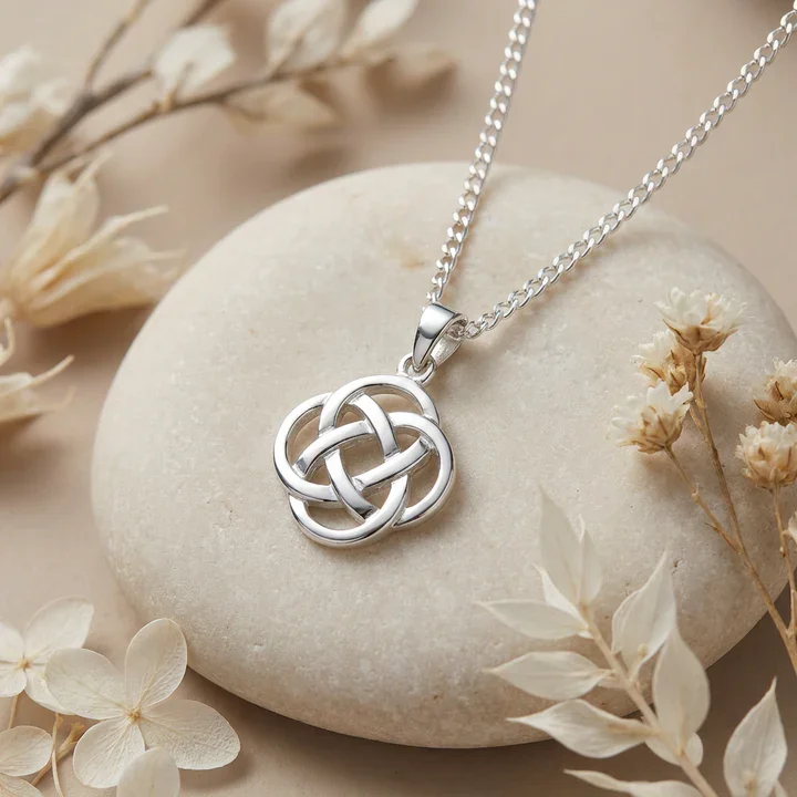 Sterling silver Celtic knotwork round pendant, four-lobed interlaced design, displayed against sea stone with natural botanicals