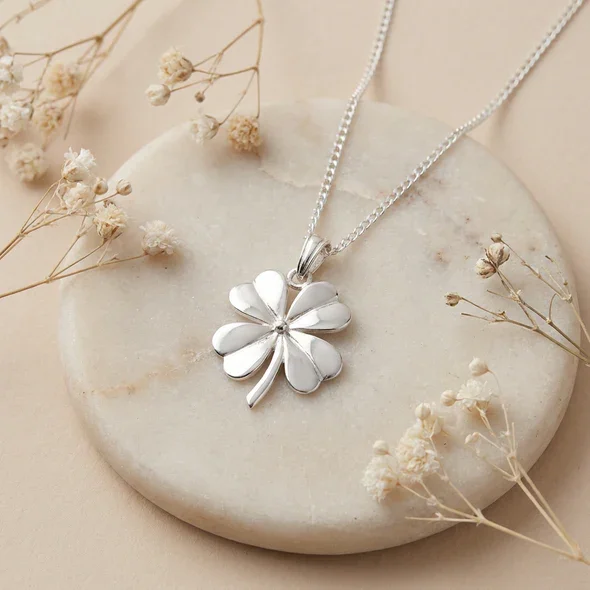 Sterling Silver Four Leaf Clover Pendant, sculpted four-lobe form, high mirror polish, shown on sea stone with dried botanicals