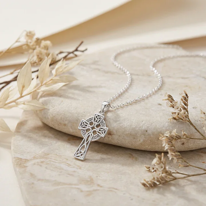 Sterling Silver Celtic cross pendant, flared crosshead with Trinity knot quadrants, shown on sea stone with dried botanicals