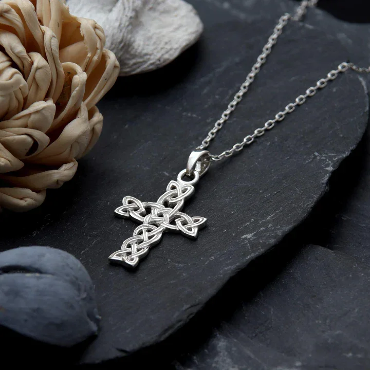 Large Sterling Silver Celtic cross pendant with open plaitwork knotwork, shown on chain against dark Scottish slate with natural botanicals
