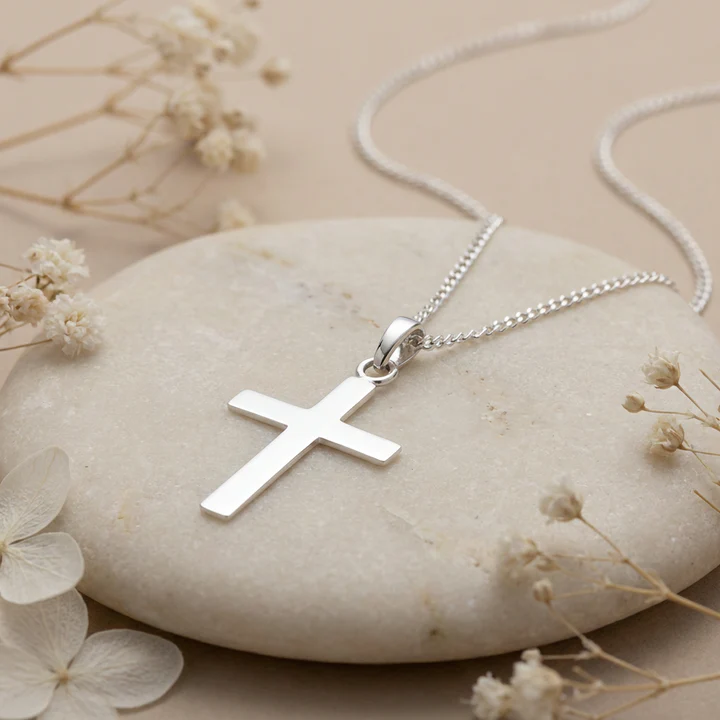 Lightweight Sterling Silver plain polished latin cross pendant, shown on light stone with natural botanicals