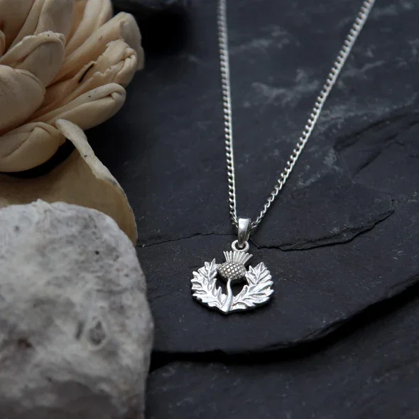 Sterling Silver Scottish Thistle Pendant, feathered head, crosshatched globe, wreath frame, shown on Scottish slate with sea stone and dried botanicals