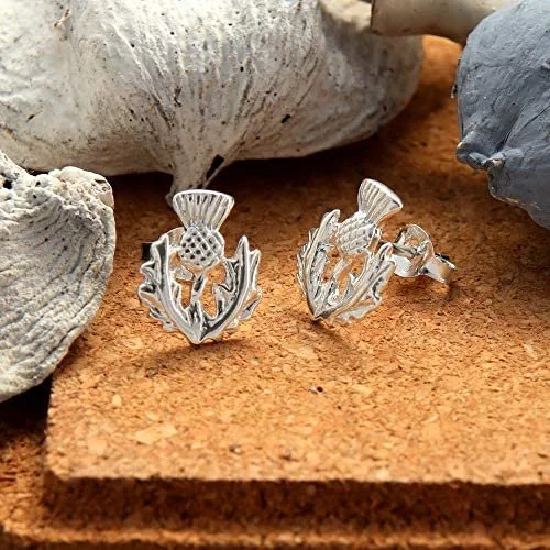Sterling Silver Scottish Thistle Stud Earrings, crosshatched globe, feathered crown, serrated leaves, 12mm x 12mm, push back fitting, shown on cork with sea stones and dried botanicals