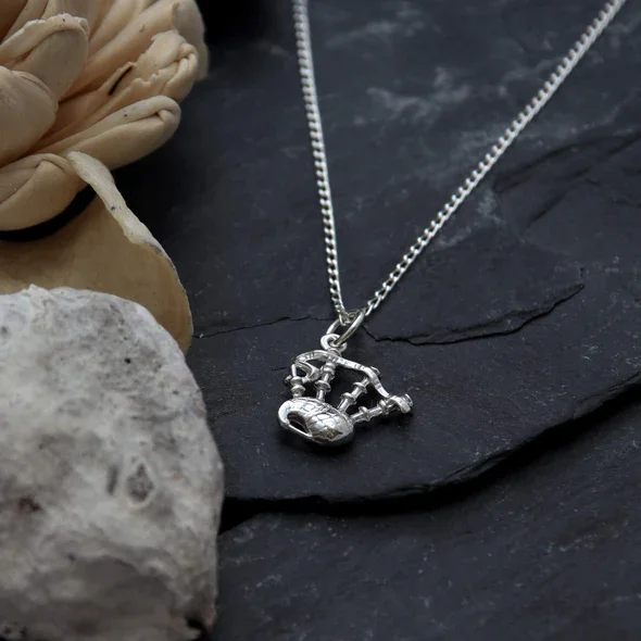 Sterling Silver Scottish Bagpipes Pendant, sculpted three-dimensional form, drone and bag detail, shown on Scottish slate with sea stone and dried botanicals