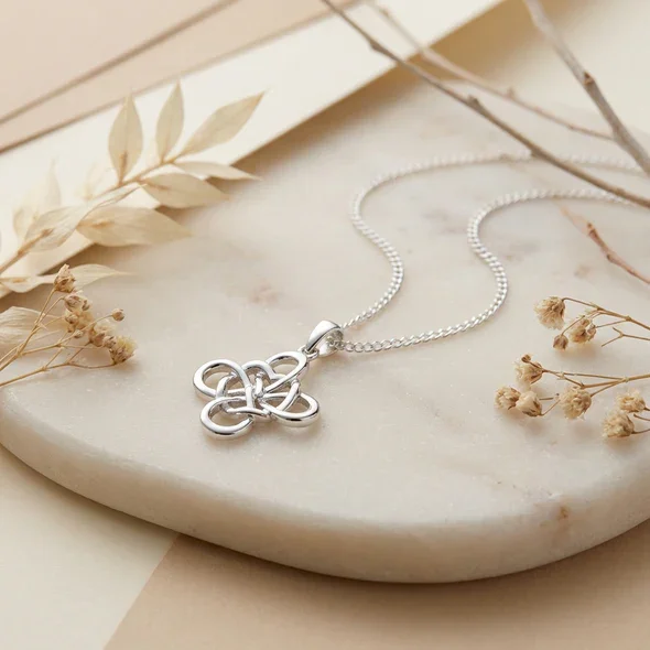 Sterling Silver Celtic Knotwork Heart Pendant, four-loop interlaced design, open heart detail, shown on sea stone with dried botanicals