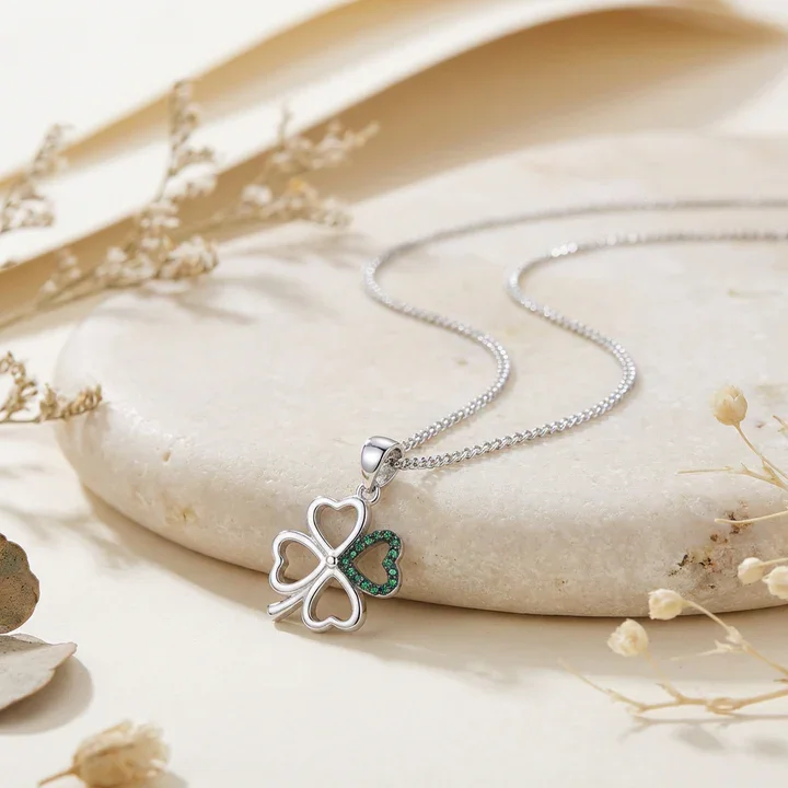 Sterling Silver Celtic Four Leaf Clover Pendant, open heart lobes, green CZ set, shown on sea stone with dried botanicals