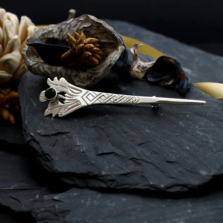 Sterling Silver Scottish thistle kilt pin with green cubic zirconia, displayed on Scottish slate with dried botanicals