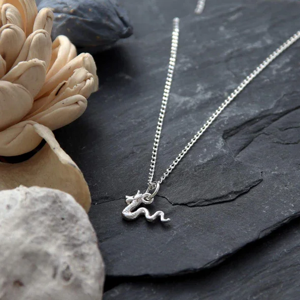 Sterling Silver Loch Ness Monster Pendant, sinuous serpentine form, scaled texture, shown on Scottish slate with sea stones and dried botanicals