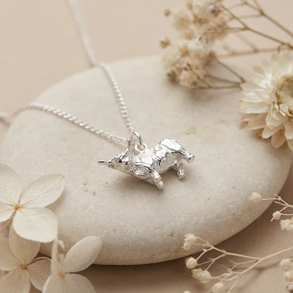 Sterling Silver Scottish Highland Cow Pendant, sculpted three-dimensional form, engraved coat detail, shown on sea stone with dried botanicals
