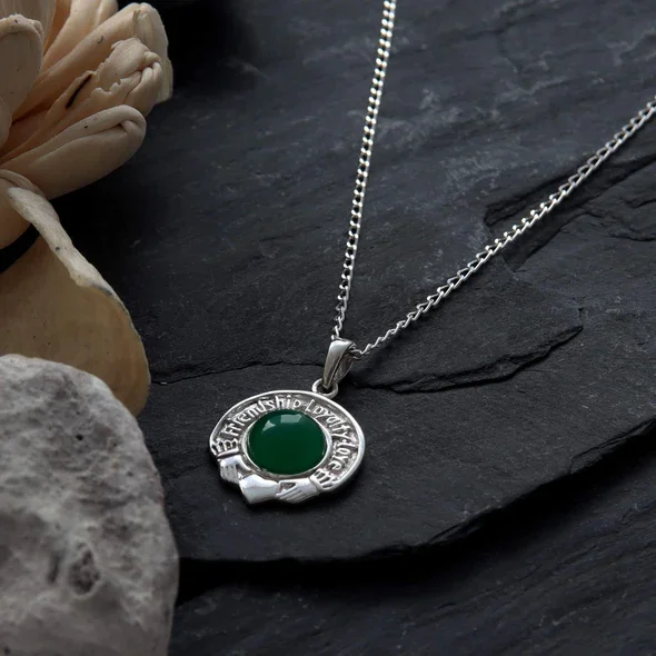Sterling Silver Claddagh Pendant, engraved Friendship Loyalty Love border, green CZ bezel set, shown on Scottish slate with sea stone and dried botanicals