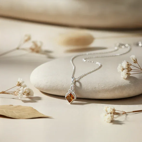 Sterling Silver Celtic Knotwork Pendant, natural amber square-cut stone, bezel set, shown on sea stone with dried botanicals