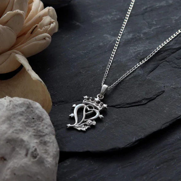 Sterling Silver Scottish Luckenbooth Pendant, crowned intertwined hearts, thistle detail, shown on Scottish slate with sea stones and dried botanicals