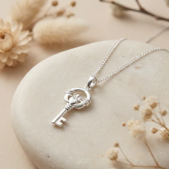 Sterling Silver Claddagh Key Pendant, hands heart and crown motif, high mirror polish, shown on sea stone with dried botanicals