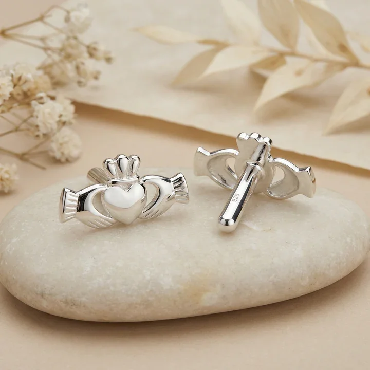 Sterling Silver Claddagh cufflinks. Sculptural hands, ribbed cuffs, crowned heart, high mirror polish, shown on sea stone with dried botanicals