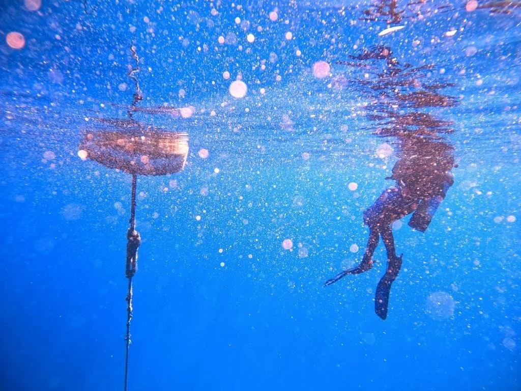 A person swimming underwater near a boat, with bubbles surrounding them.