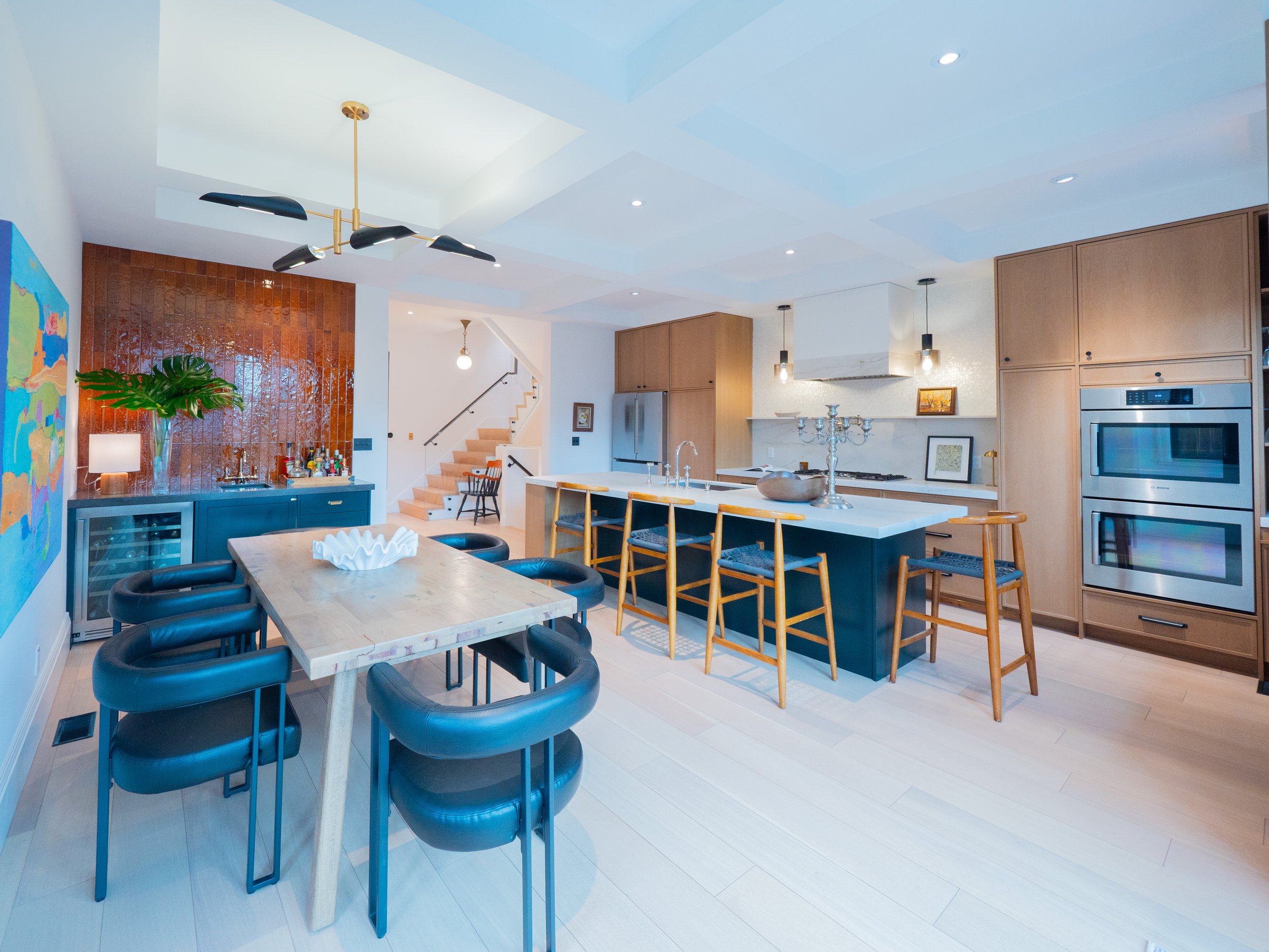 Modern open-concept kitchen and dining area with a wooden table, black chairs, a kitchen island with wooden barstools, stainless steel appliances, and decor.