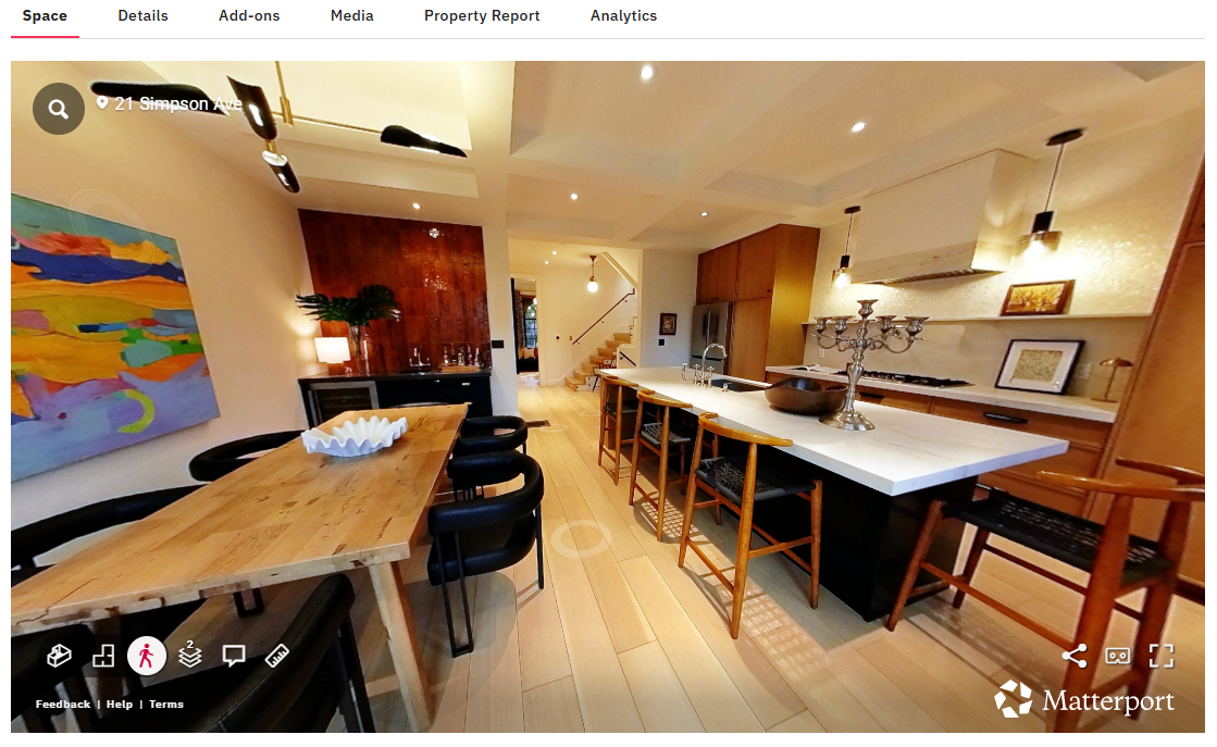 Open-concept kitchen and dining area with wooden flooring, black and wooden chairs, abstract wall art, chandelier, and modern pendant lighting.